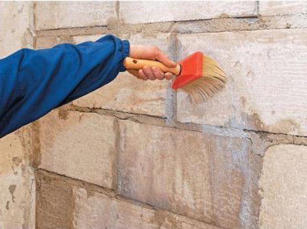 La photo montre le processus de préparation des murs de briques avec une composition spéciale, avant de les coller avec des plaques de plâtre